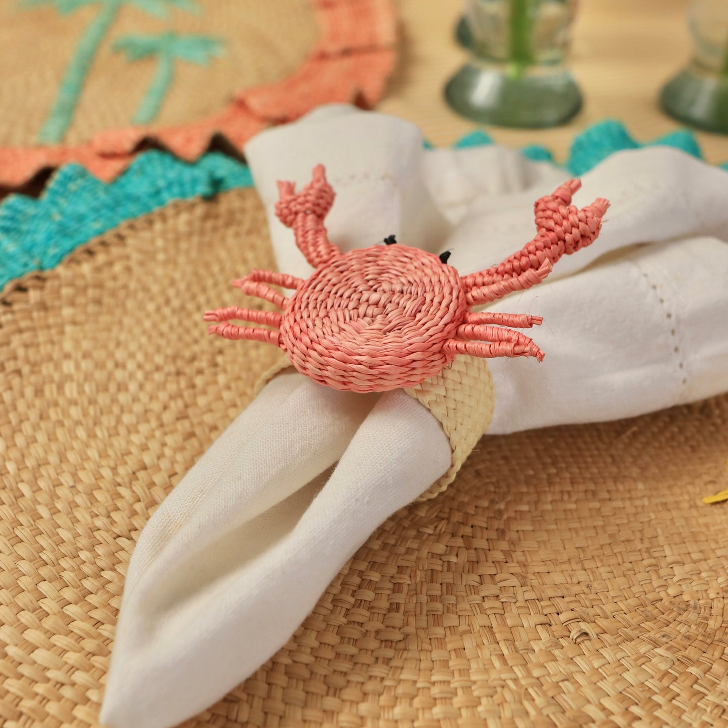 Napkin ring shaped like a crab on a woven surface with decorative elements in the background.